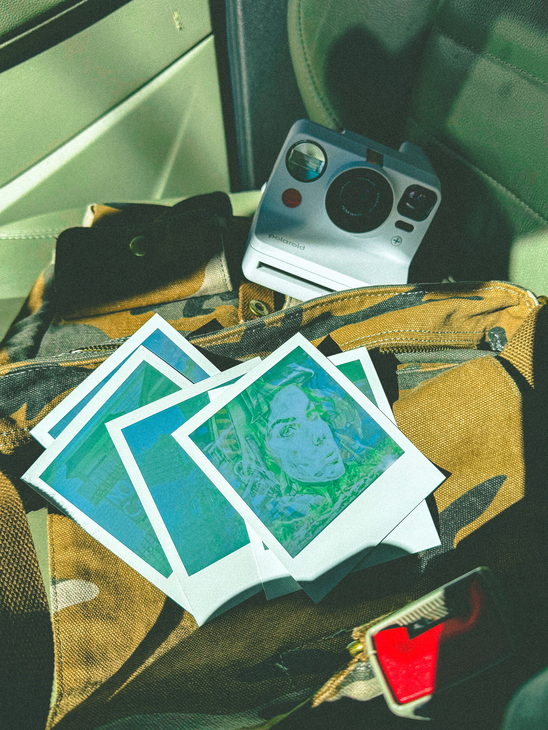 A Polaroid Now+ camera sitting in the car on top of a bag. Next to it are several Polaroids developing.